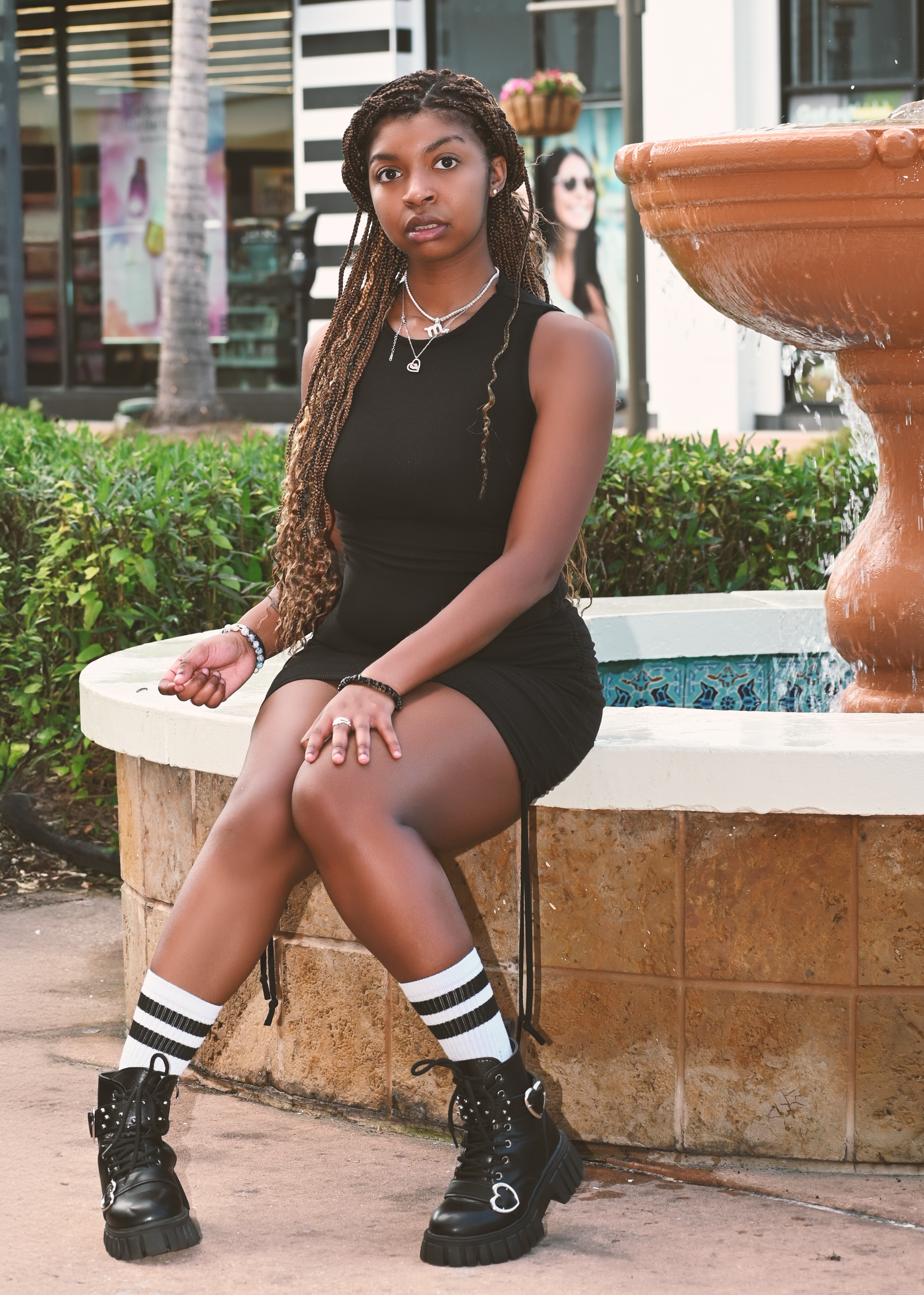 Outdoor portrait by fountain wearing black dress with combat boots and striped socks.