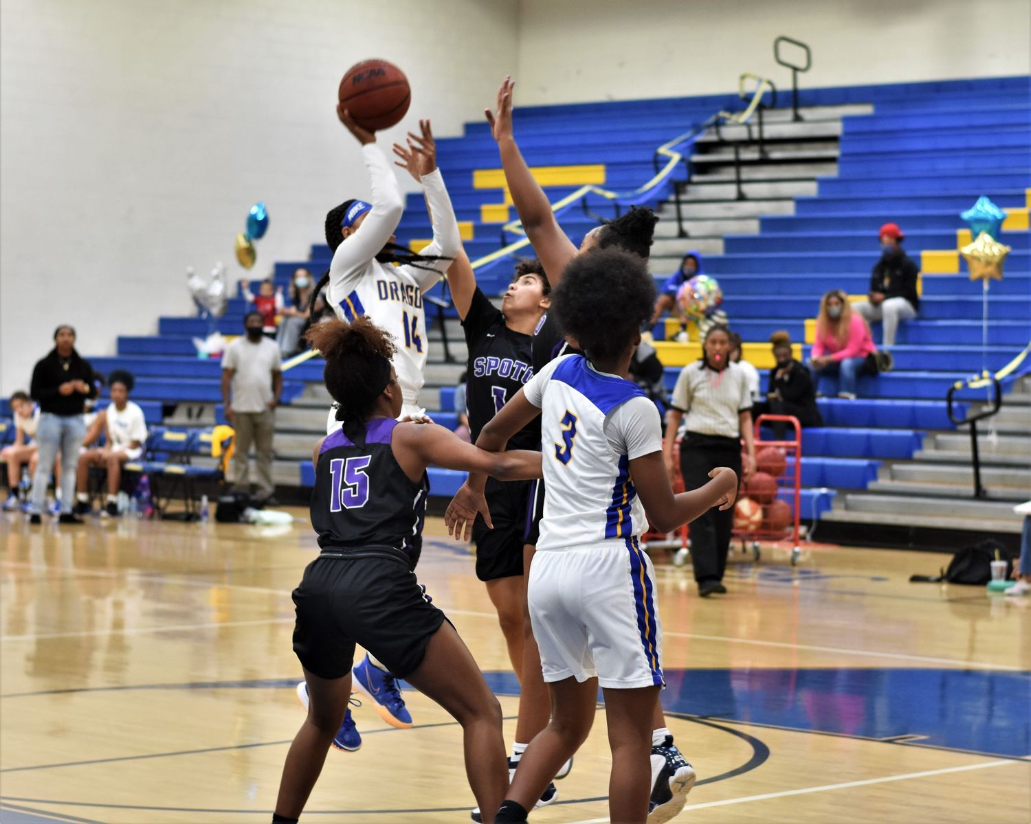Basketball players compete in an indoor gymnasium with blue bleachers.