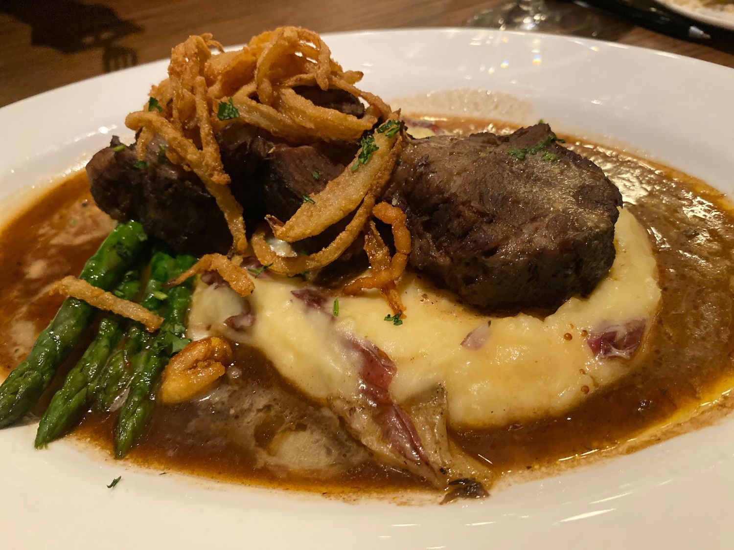 Braised meat dish with sauce and garnishes on a white plate.