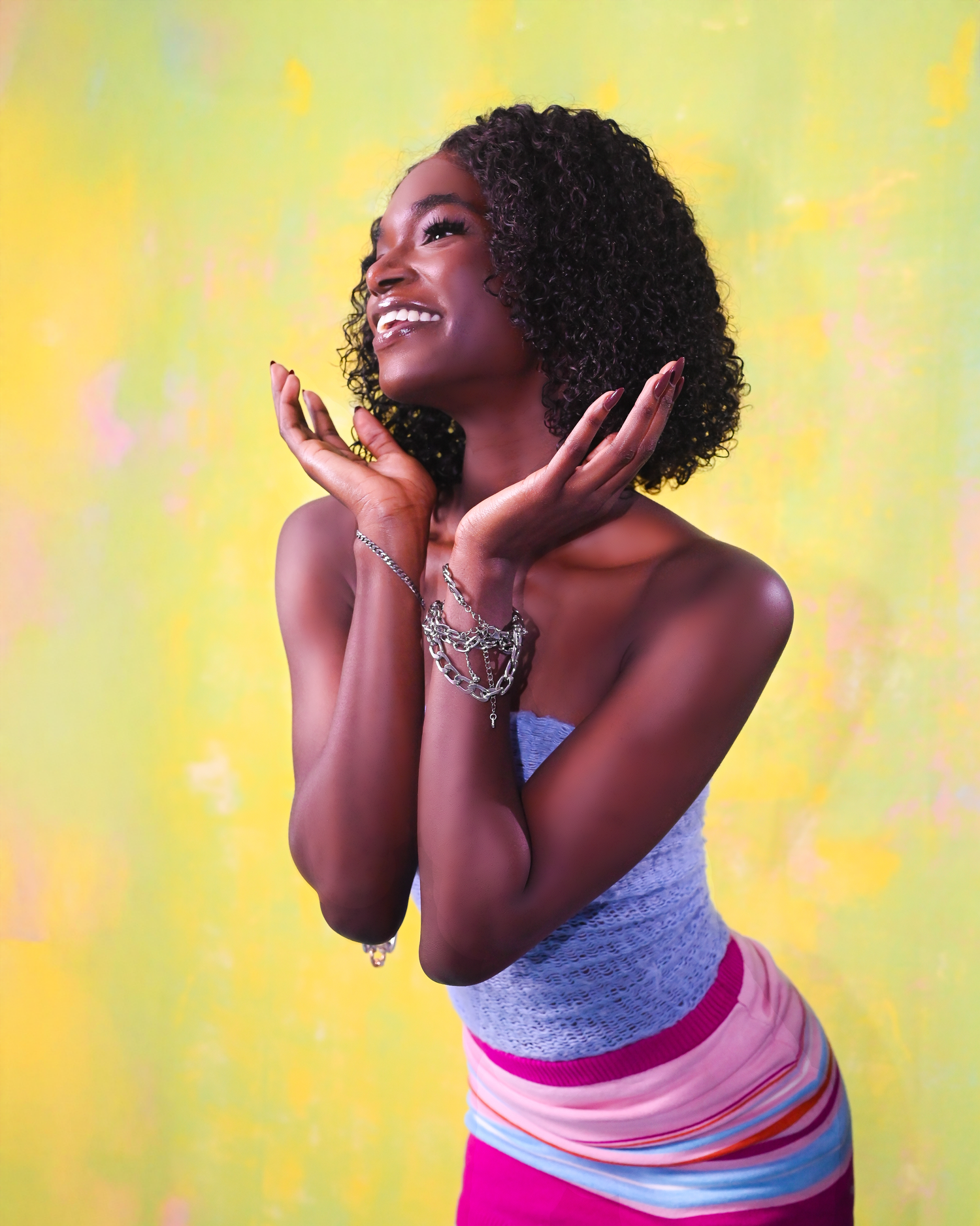 Joyful fashion portrait in grey top and pink skirt against yellow-green background.