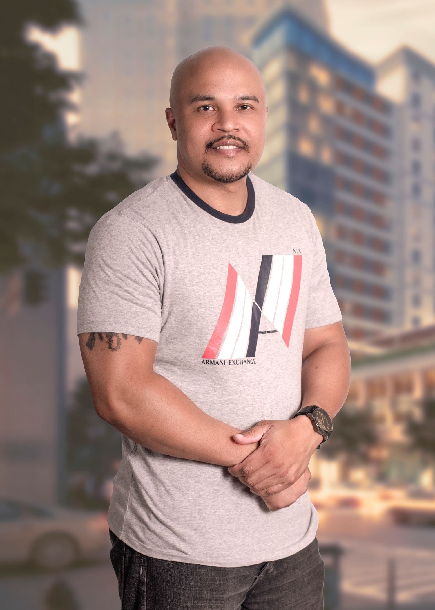 Portrait of person in grey t-shirt with graphic design standing in front of urban building backdrop.