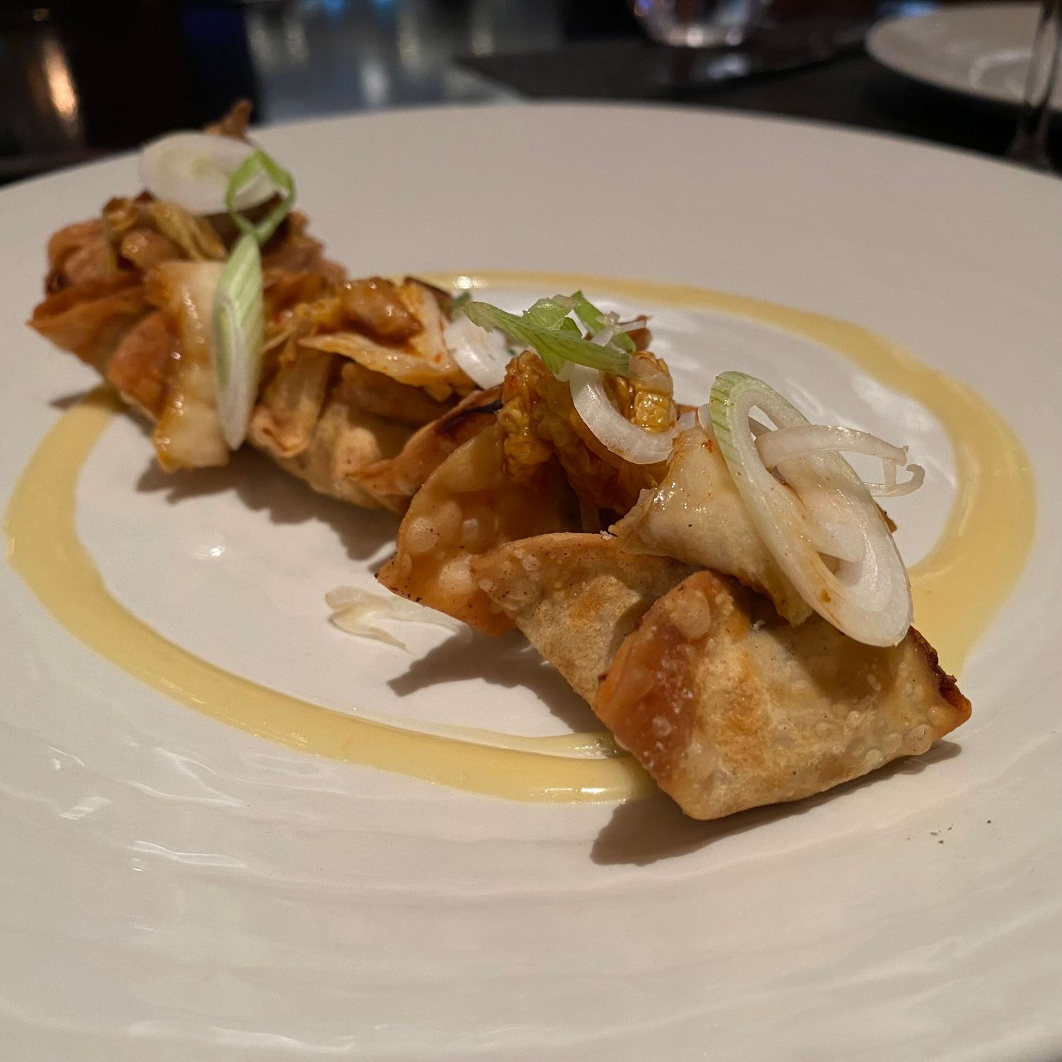 Crispy egg rolls drizzled with sauce and garnished with fresh herbs on white plates.