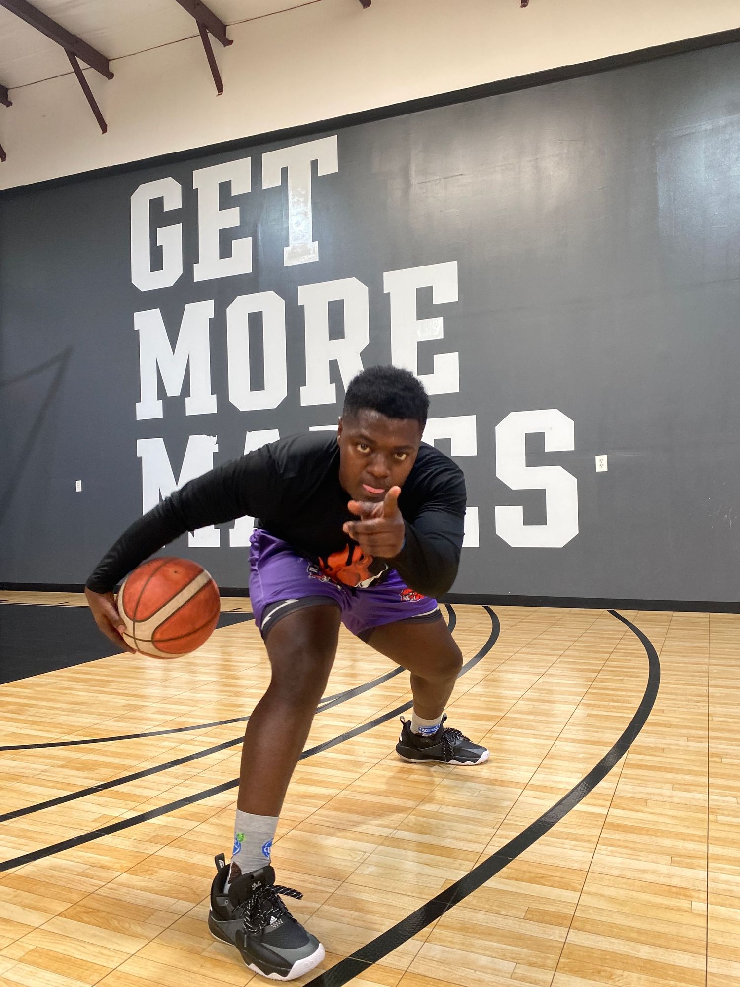 Basketball player crouching with ball on indoor court in front of motivational wall text.