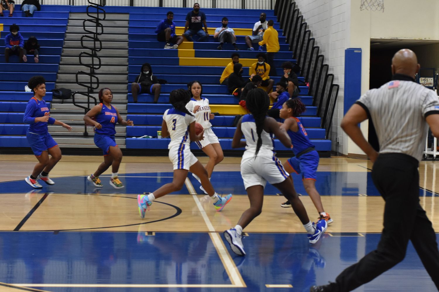 Basketball players compete in a blue and white gymnasium during an intense game.
