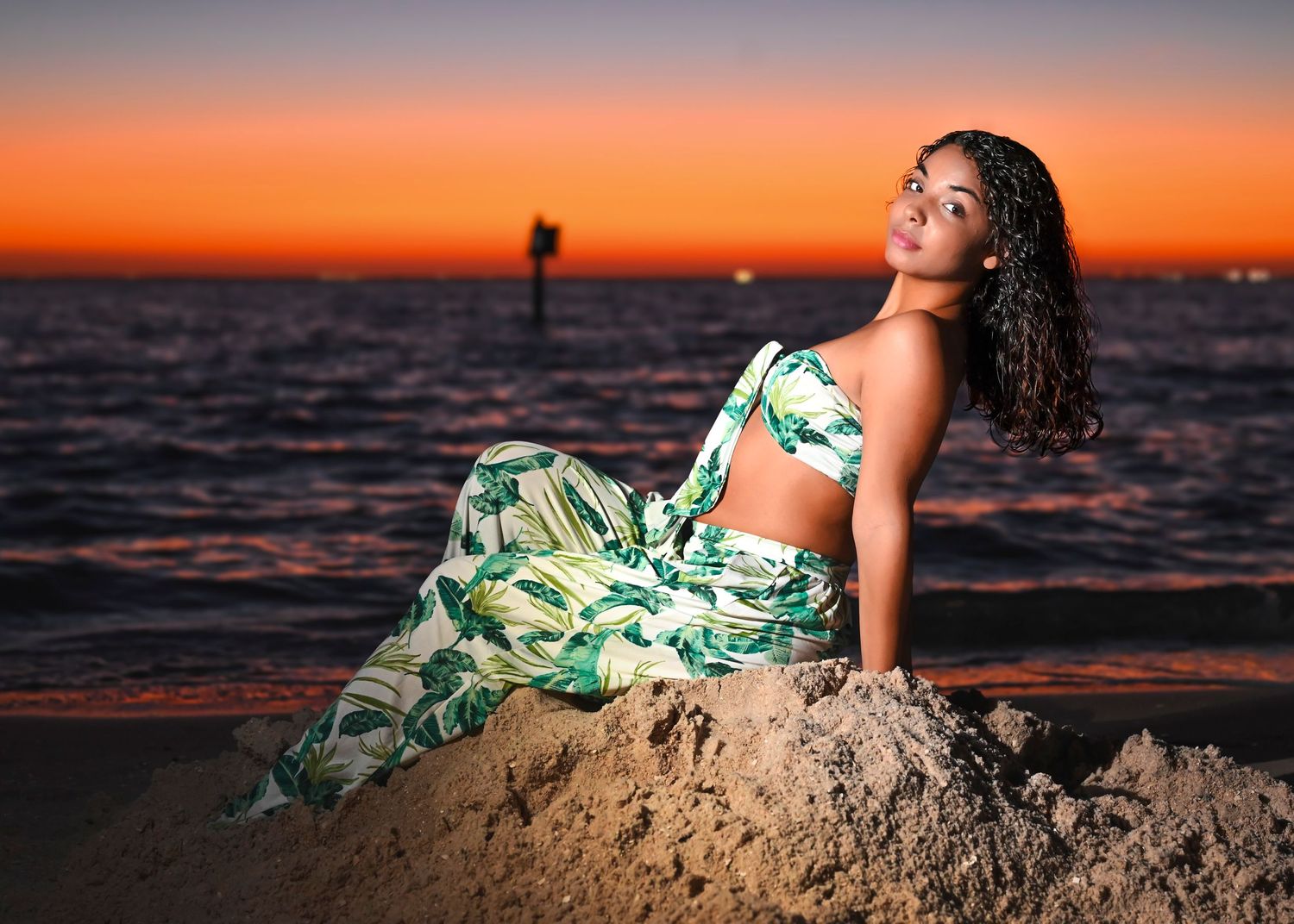 Sunset beach pose on sand with tropical print outfit and dramatic orange sky.