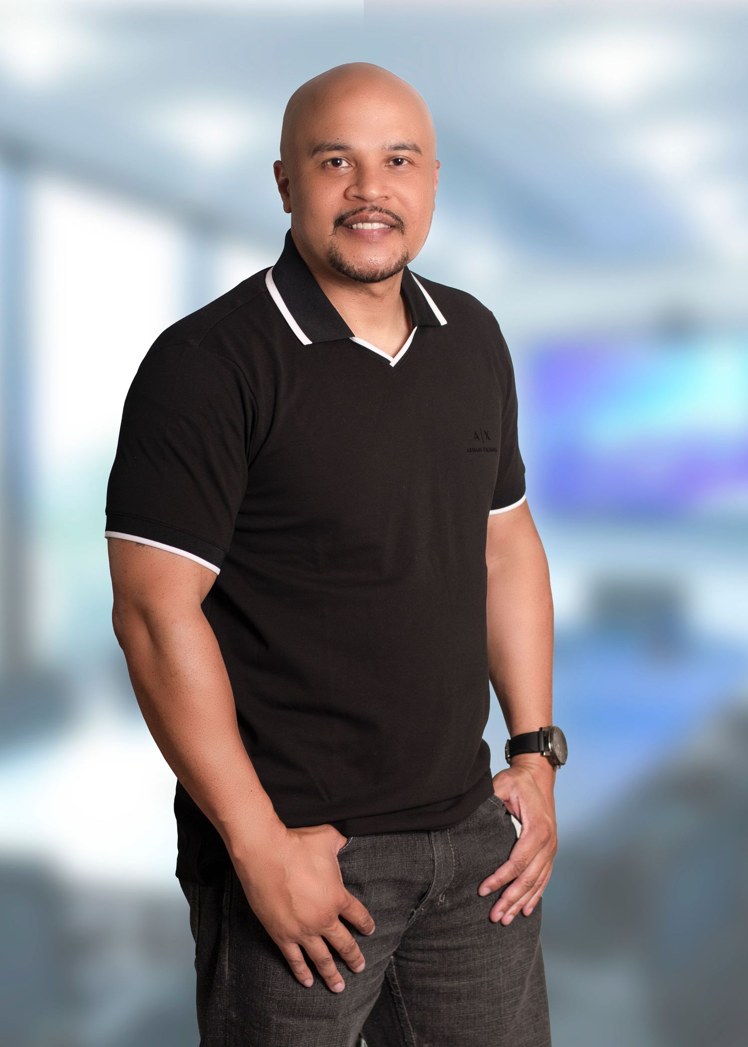 Professional headshot wearing a black polo shirt with white trim against blurred office background.