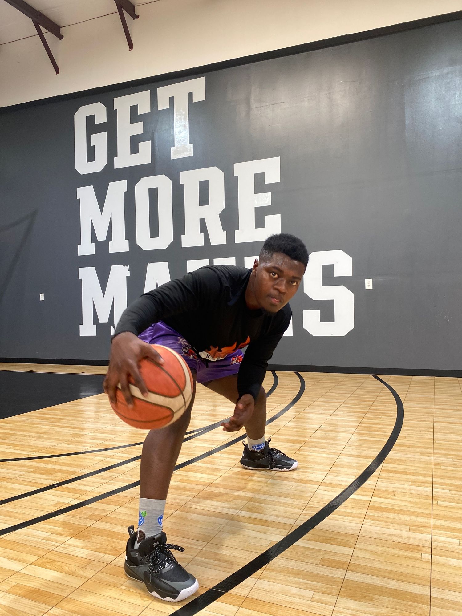 Close-up of basketball player dribbling on wooden court with motivational text on wall.