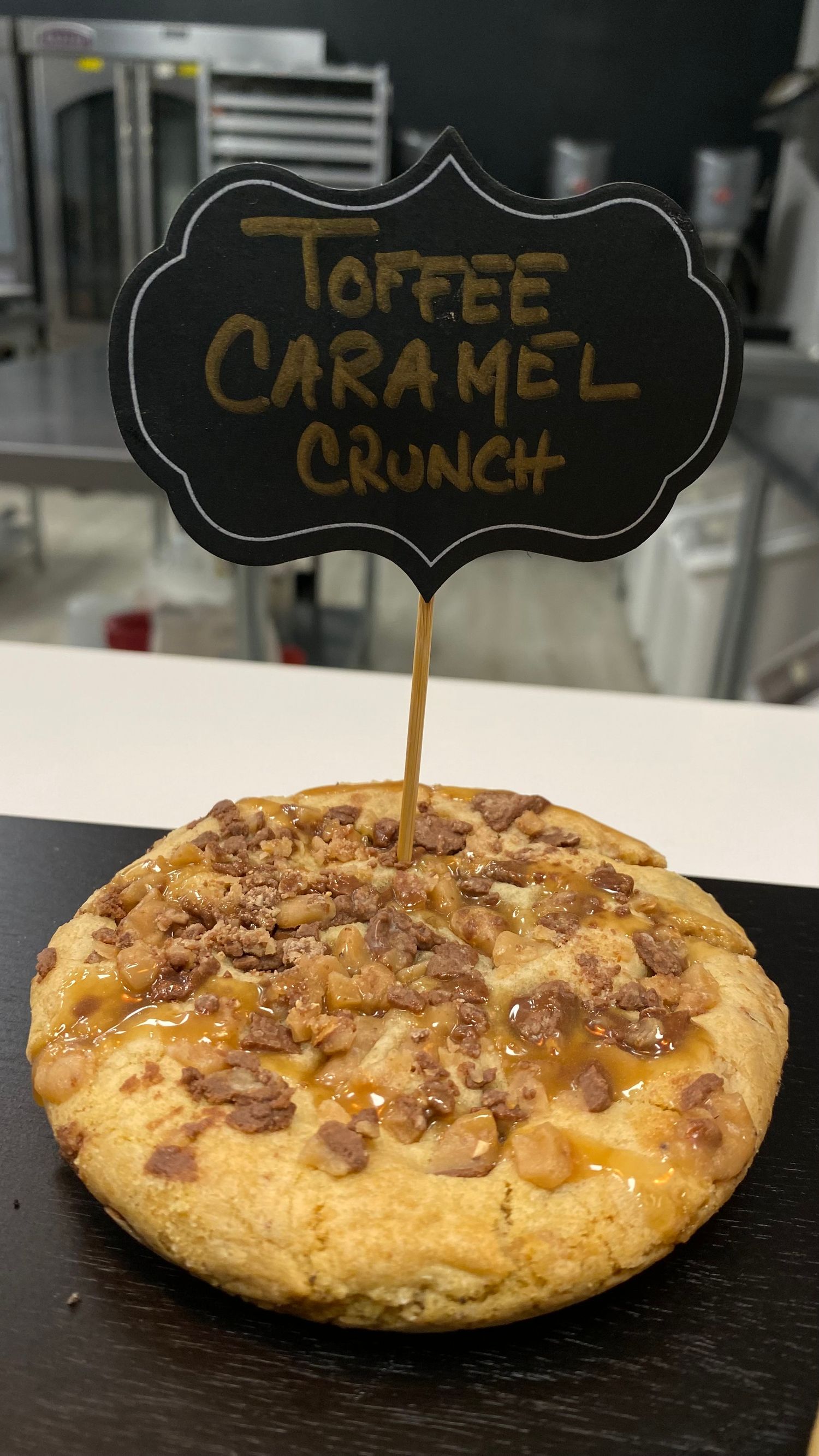 Close-up of a caramel crunch cookie with toffee bits and a decorative name tag.