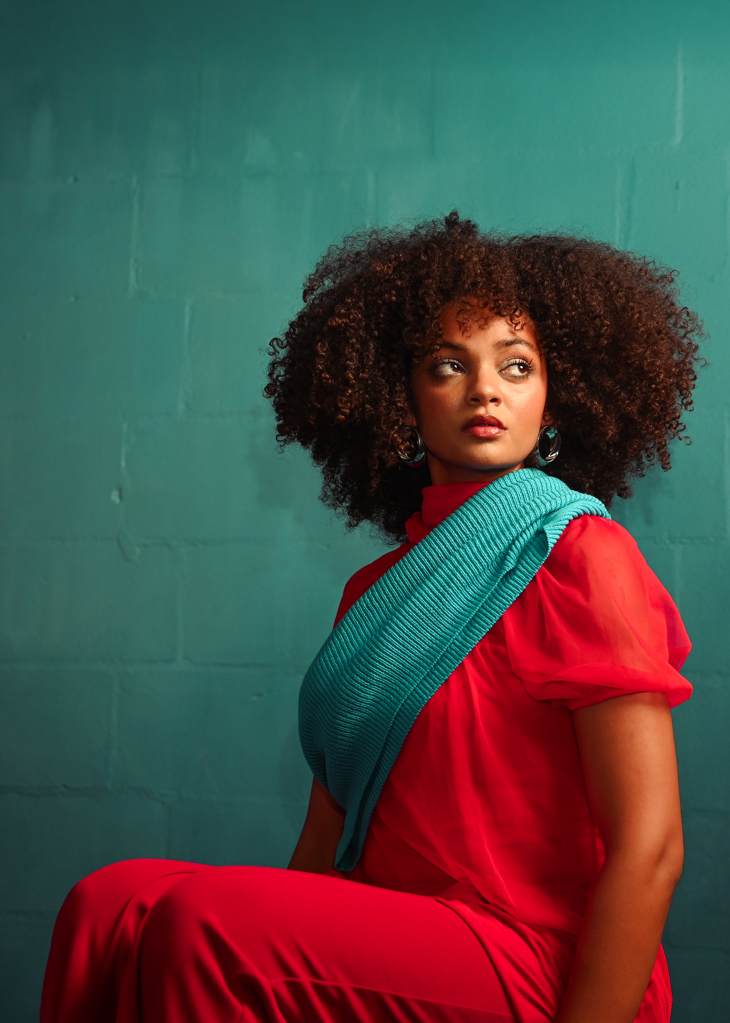 Artistic fashion photo of model in red dress against teal wall.