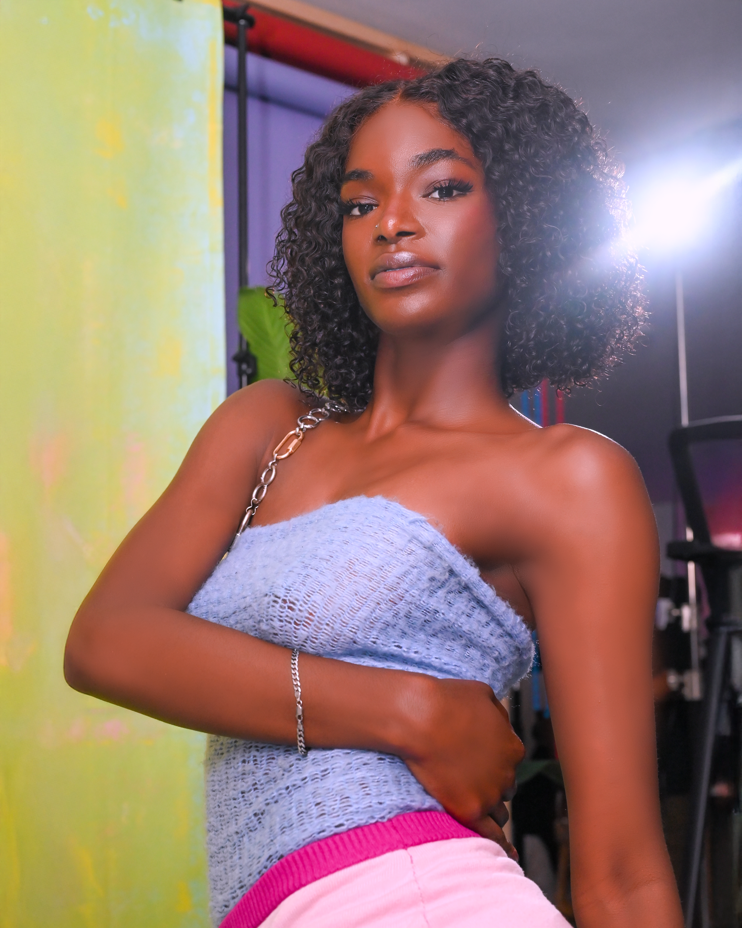 Model in purple top poses against yellow wall in studio setting.