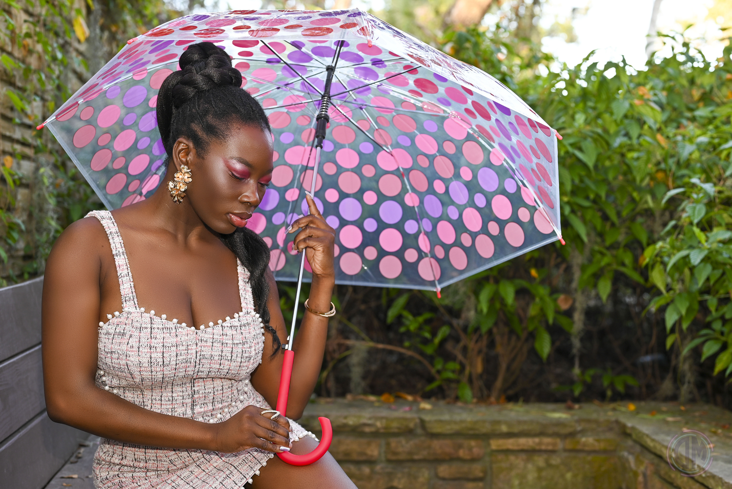 Person in white dress holding colorful polka dot umbrella in garden setting.