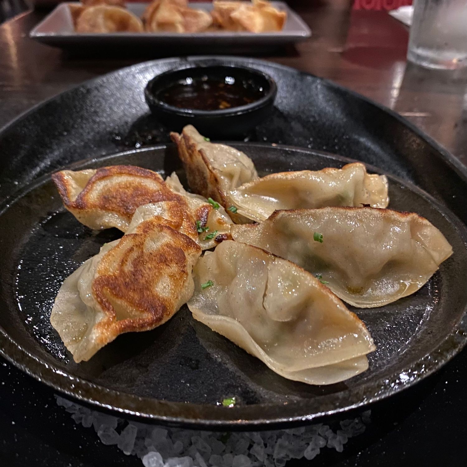 Pan-fried dumplings with crispy bottoms served on a black plate.