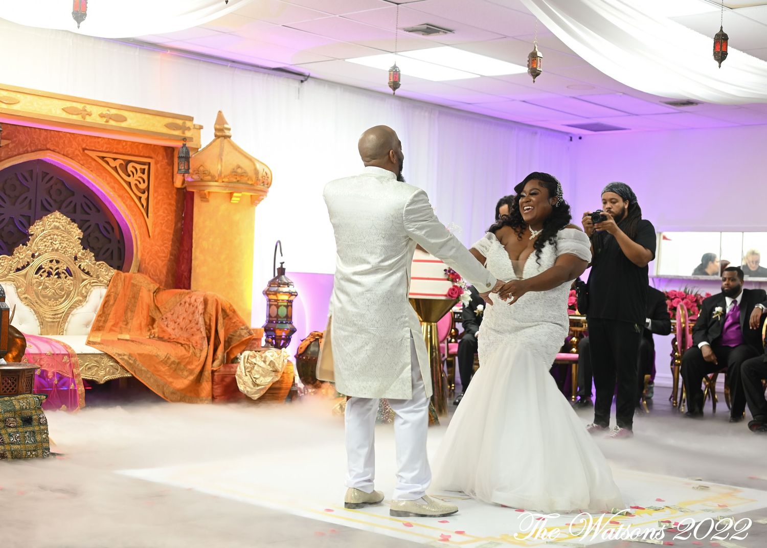 Bride and groom share first dance at elegant wedding reception with purple lighting and ornate gold throne backdrop.