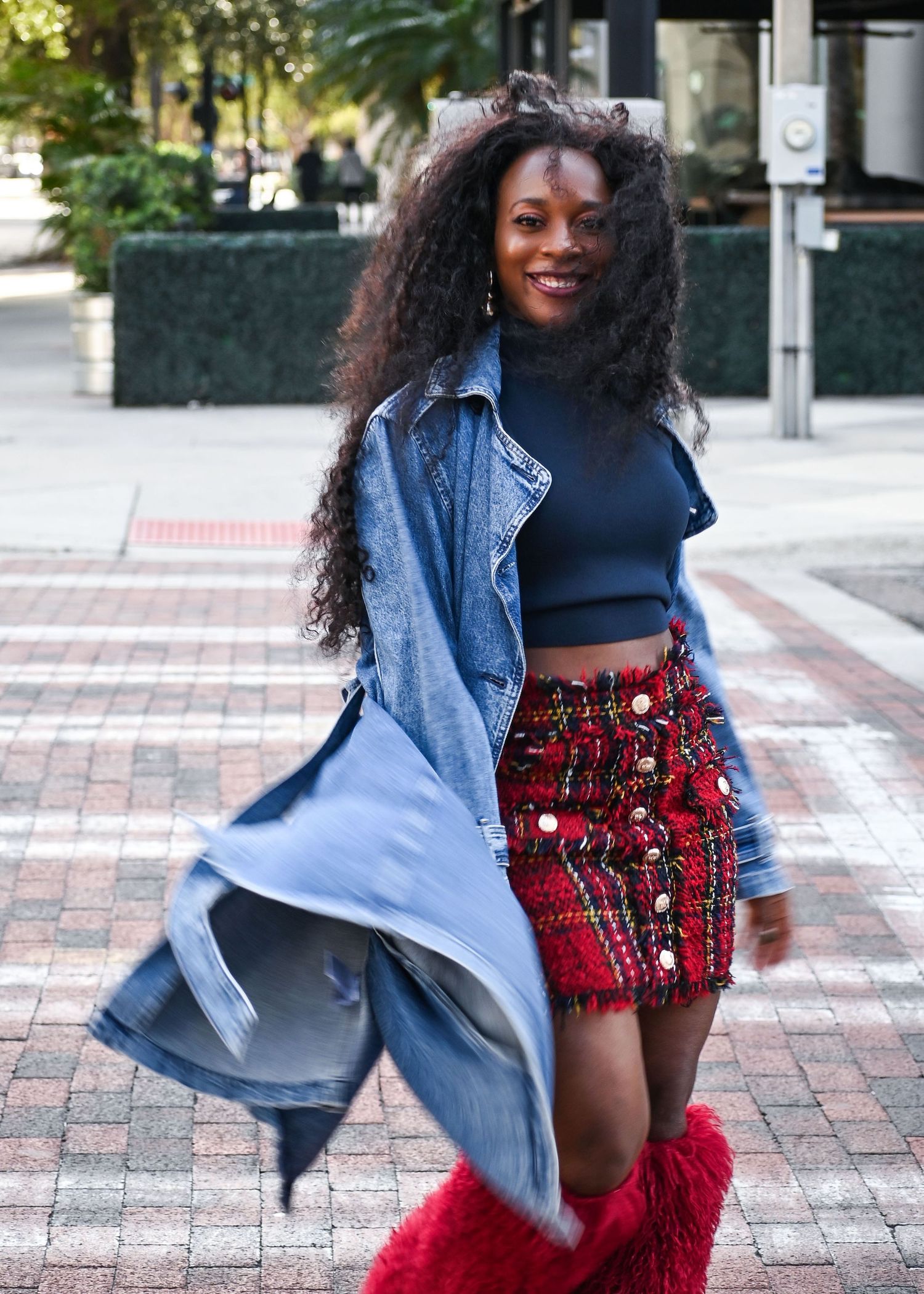 Street style fashion with denim jacket, crop top, red patterned skirt and fuzzy red boots.