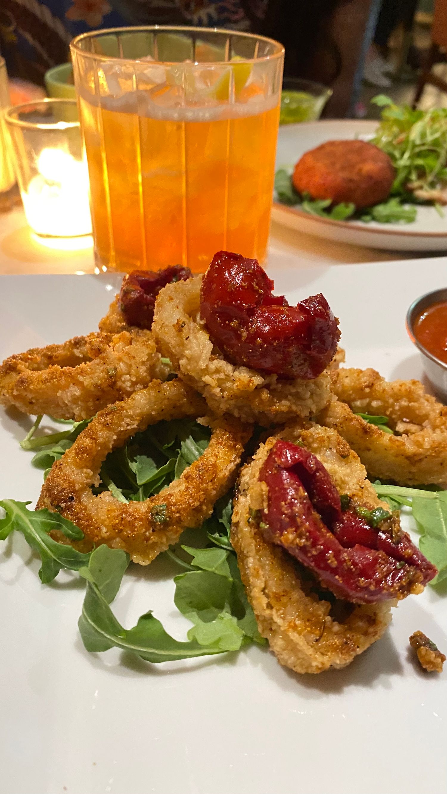 Crispy breaded appetizers garnished with arugula and red sauce on a white plate.
