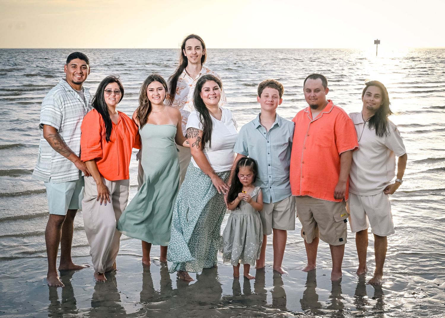 Large family group posing together on a beach at sunset, standing in shallow water with smiles.