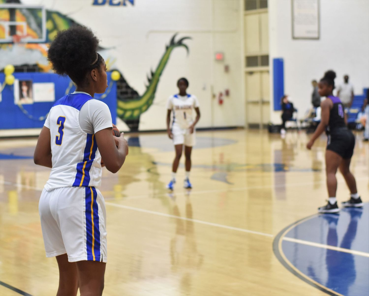 Basketball players in white uniforms practice drills in a gymnasium.