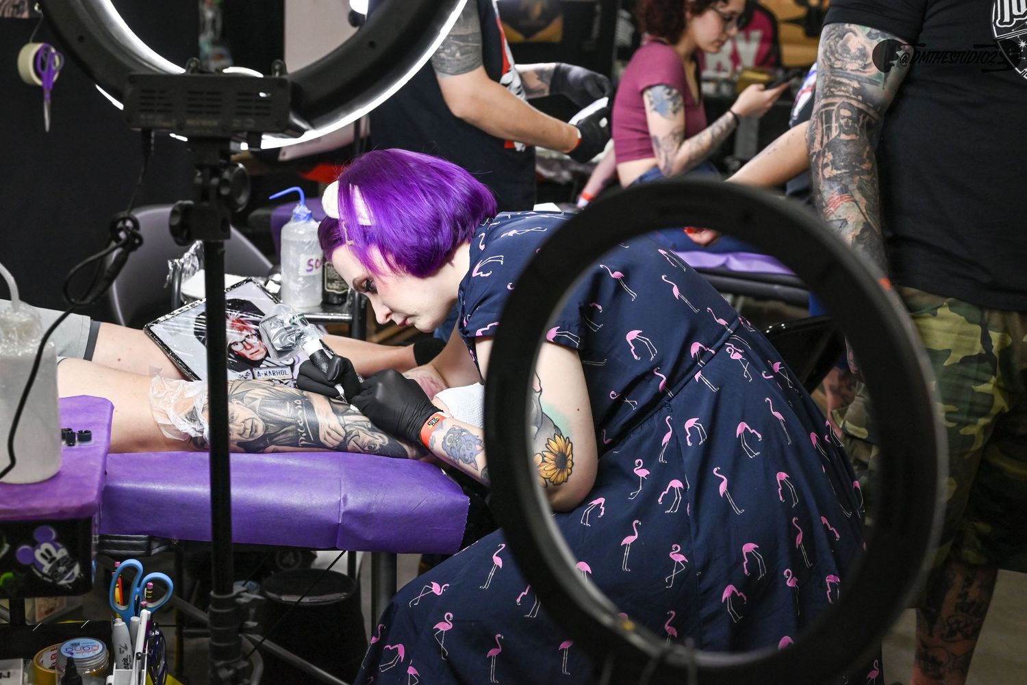 Tattoo artists working on clients in professional chairs at convention stations.
