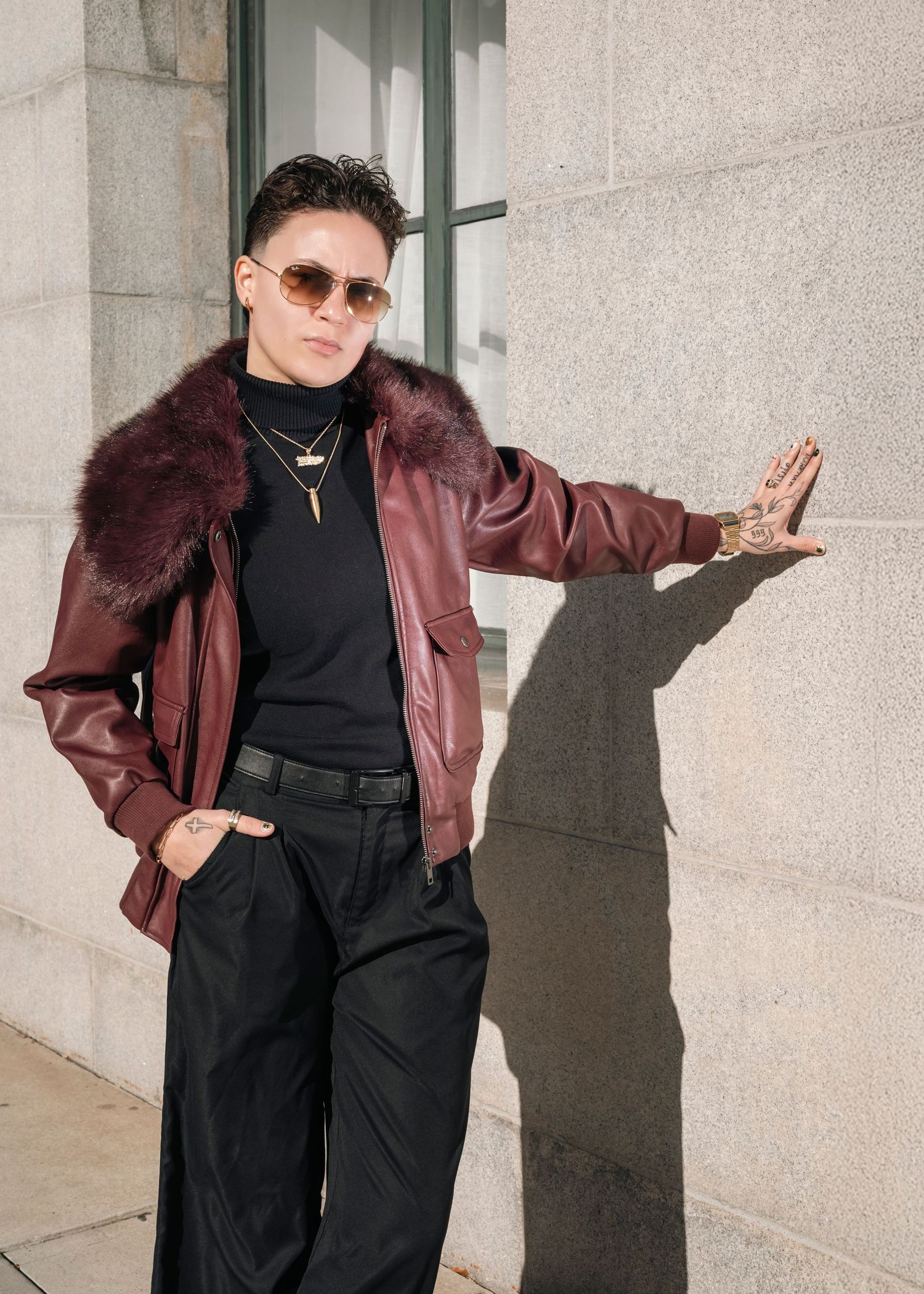 Stylish outfit featuring burgundy leather jacket and black pants photographed against concrete wall.