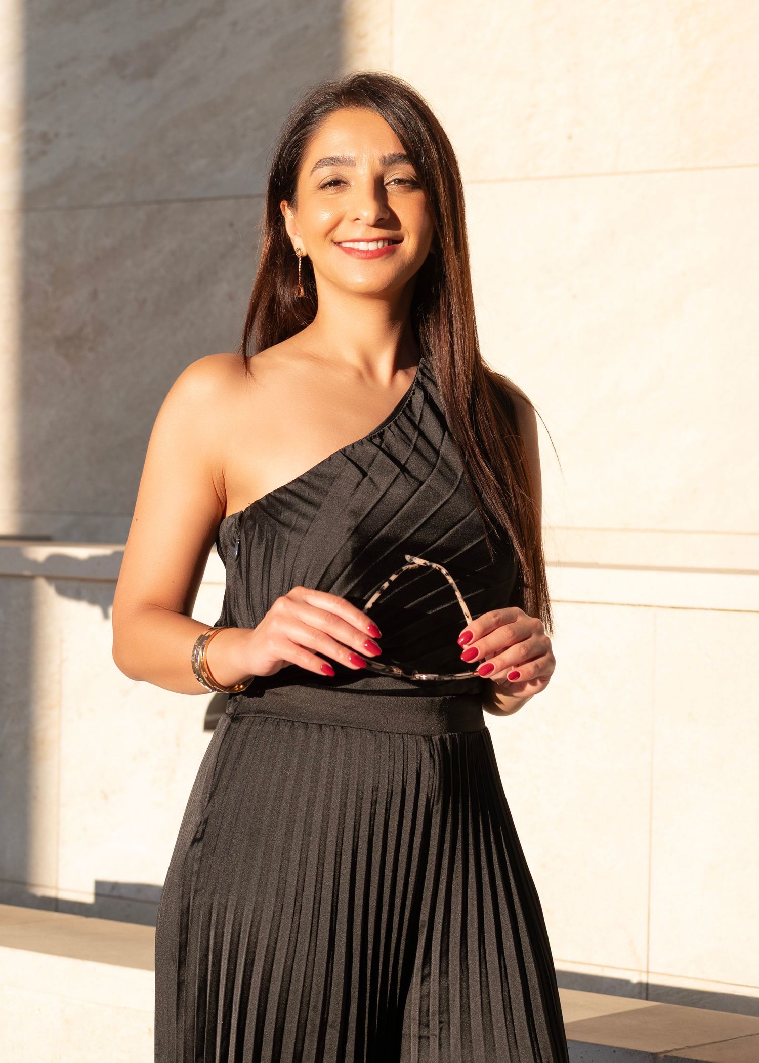 Woman wearing one-shoulder black pleated dress smiling at camera.