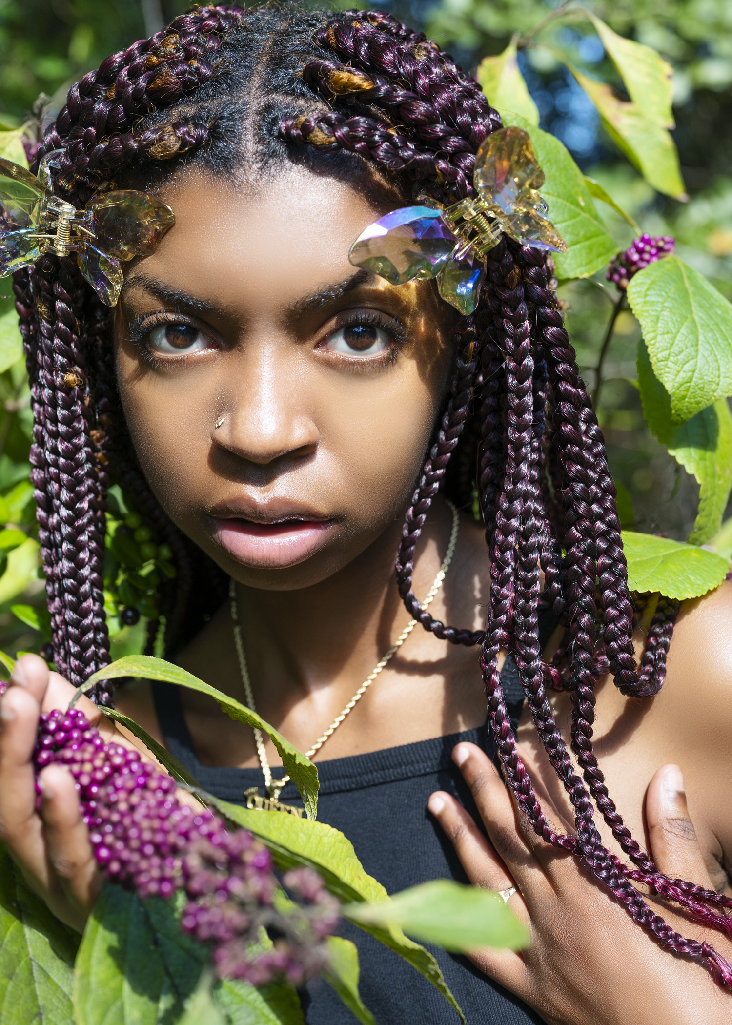 Natural outdoor portrait with purple braids and foliage background.