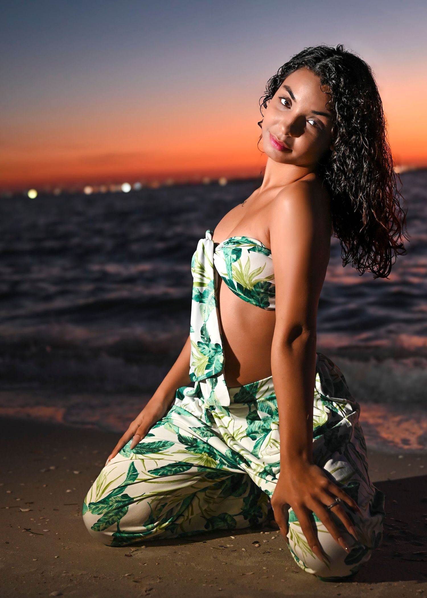 Beach photoshoot featuring tropical print outfit against vibrant orange sunset sky.