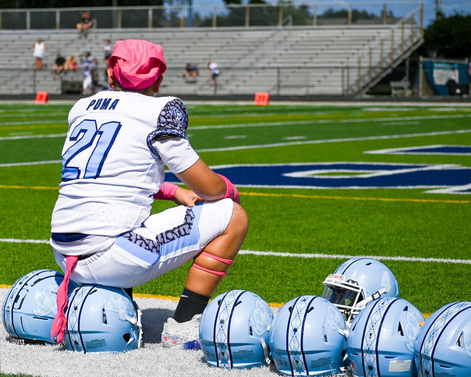 Row of light blue football helmets lined up on sports field sideline.