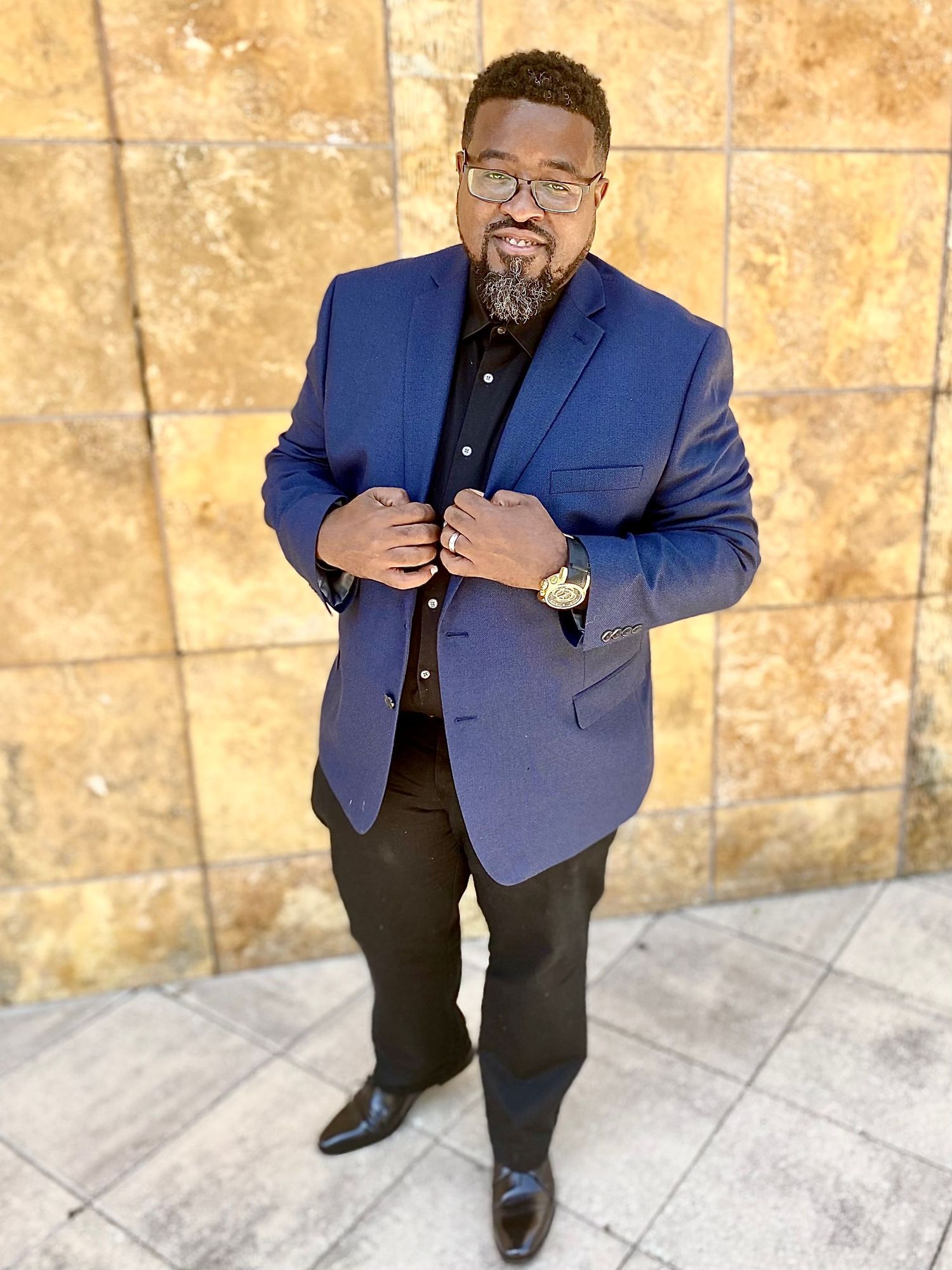 Person wearing blue blazer posing against textured wall.