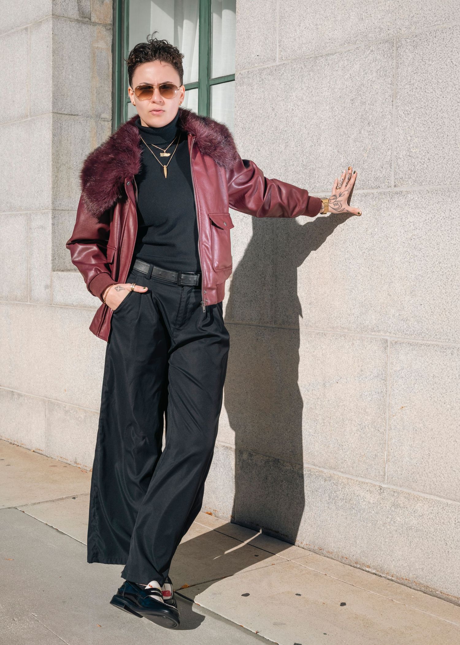 Urban fashion photoshoot with burgundy jacket and black ensemble against stone building exterior.