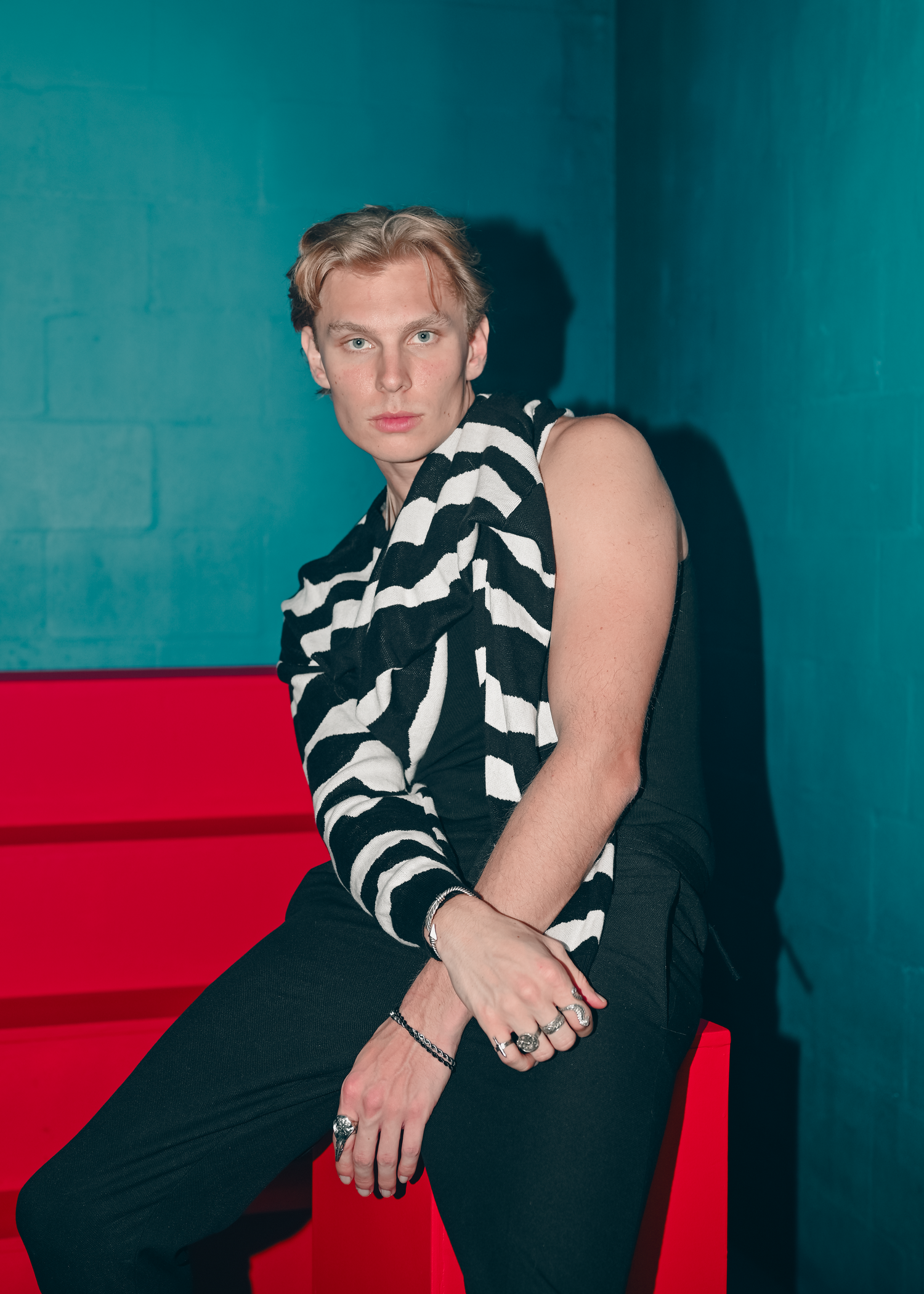 Fashion model poses against turquoise wall wearing black and white striped top in artistic portrait series.
