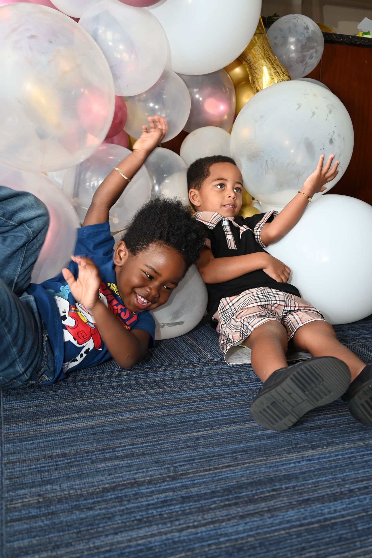Children playing and laughing while laying on striped carpet with white balloons.