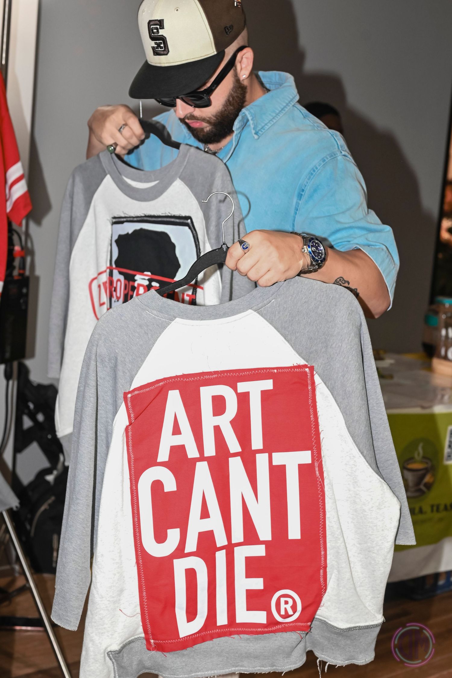 Gray sweatshirts with red 'Art Can't Die' logo text displayed at merchandise booth.