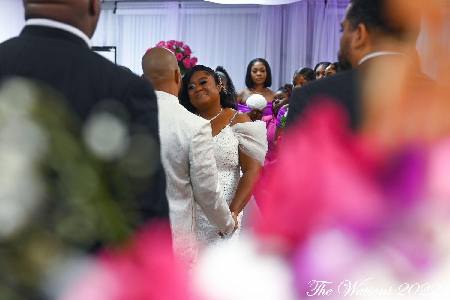 Bride in white gown gazes forward during wedding ceremony surrounded by guests in elegant decorated venue.