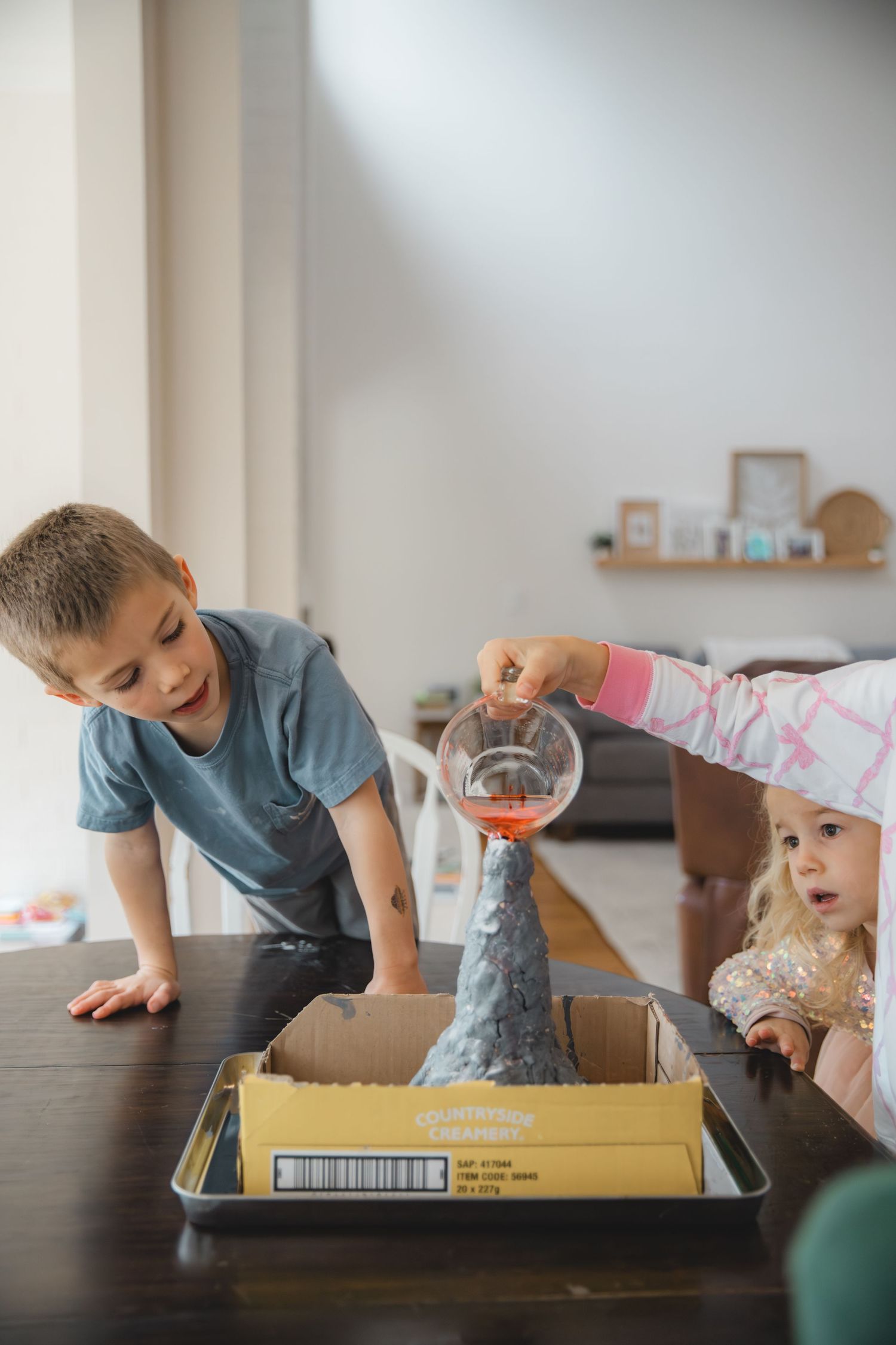 pouring mixture into homemade volcano, homeschooling experiment, child looking to see what happens