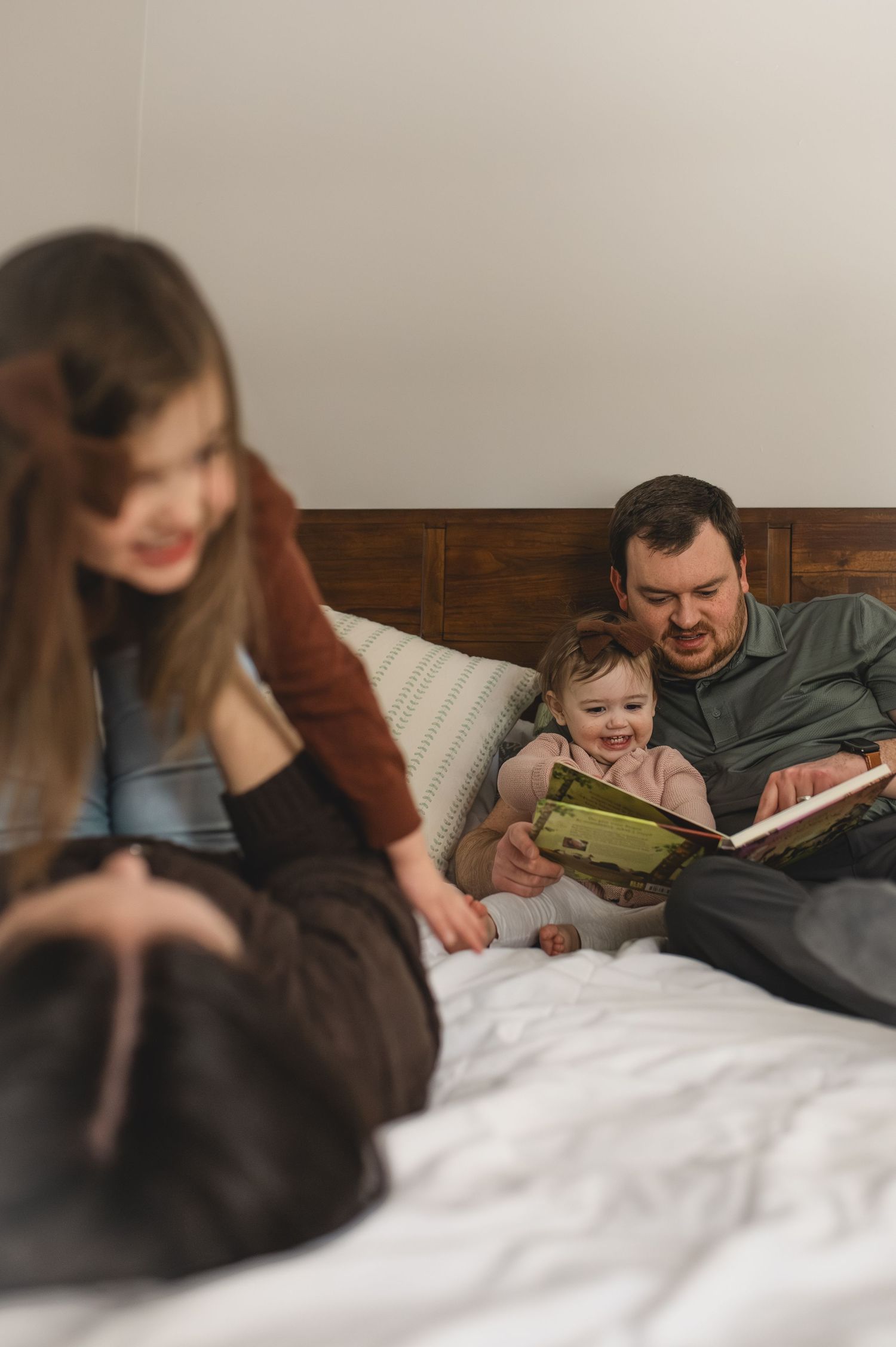 dad and toddler reading book, mom and preschooler playing on bed