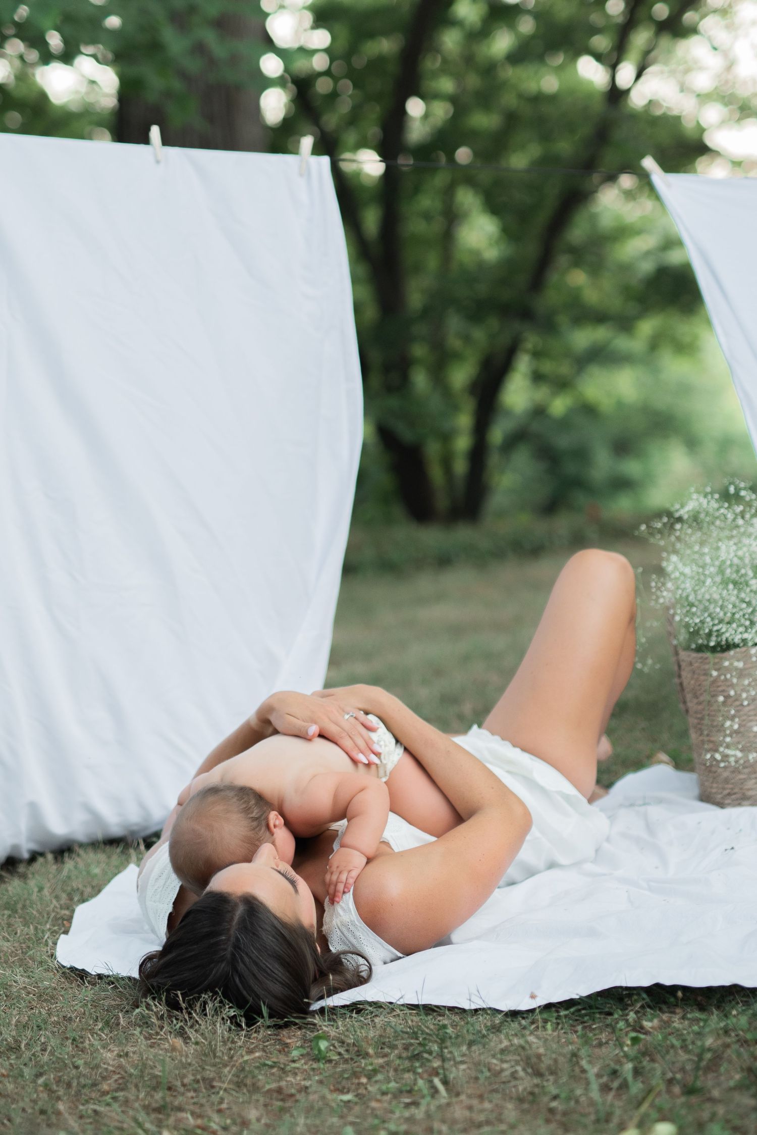 mom and baby outside laying on white sheet with clothesline hugging, baby's breath in basket