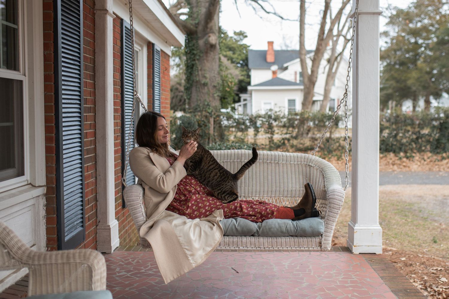 pregnant mama woman sitting on porch swing with grey brown and black cat on front porch at-home family maternity session nc