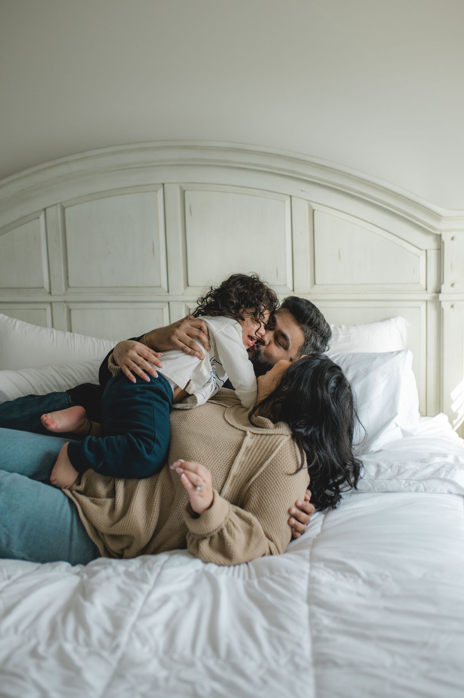 mom dad and son laying on bed, holding hands, playing, laughing, smiling