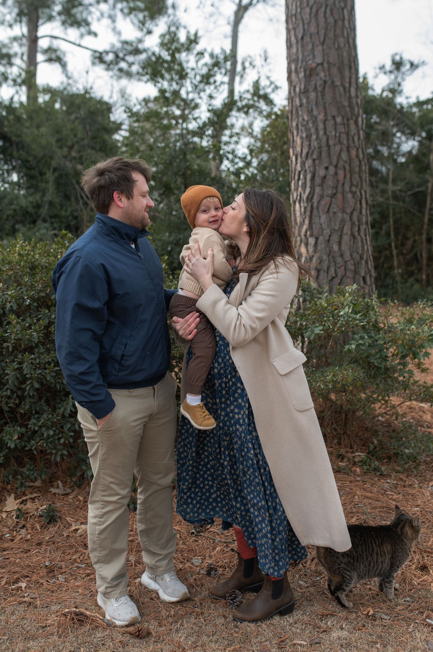 family standing in front of tree and bushes hugging, black cat