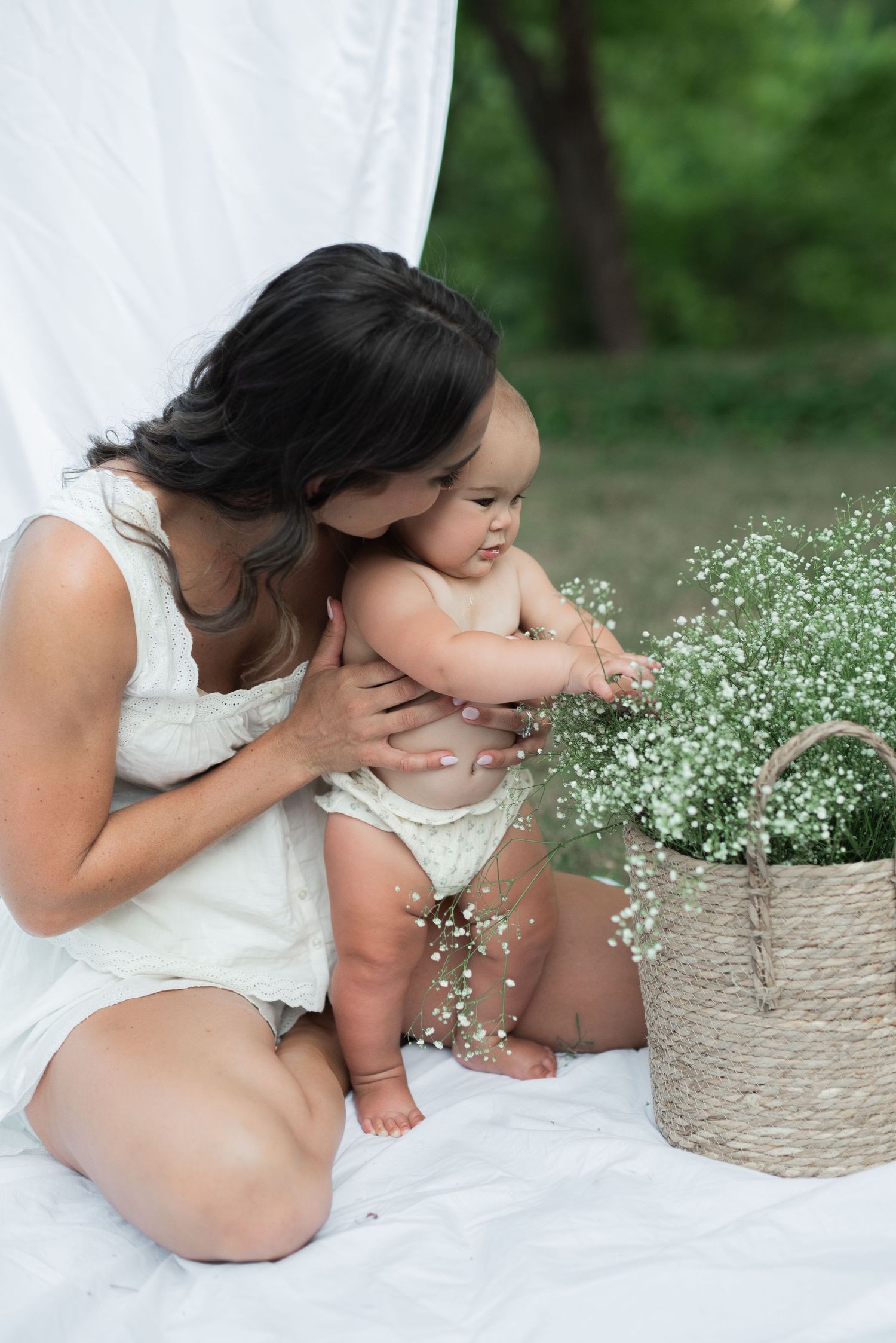mom and baby outside sitting on white sheet with clothesline hugging, baby's breath in basket