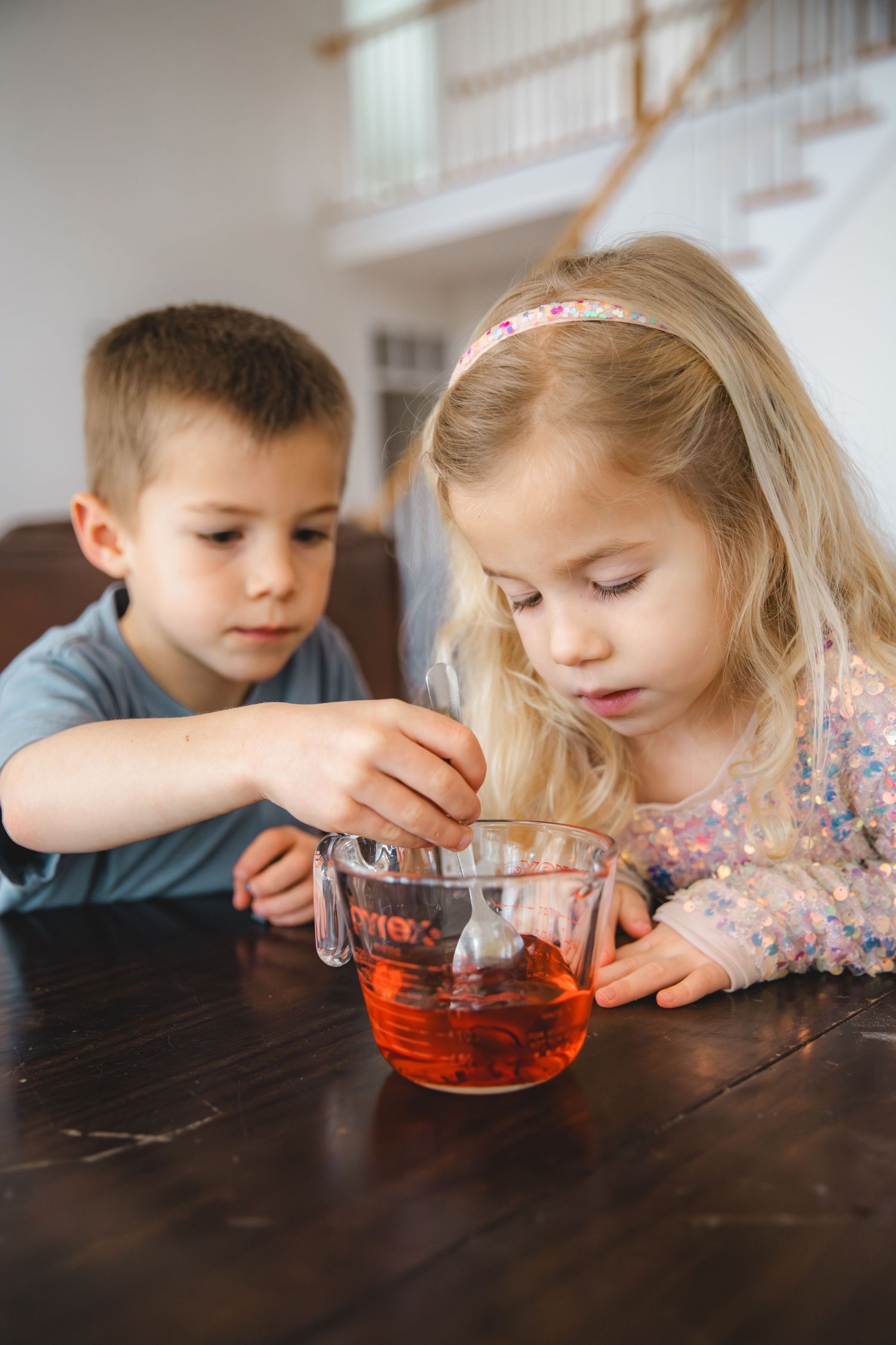 boy and girl mixing food coloring and water in a measuring cup, family experiment, homeschooling