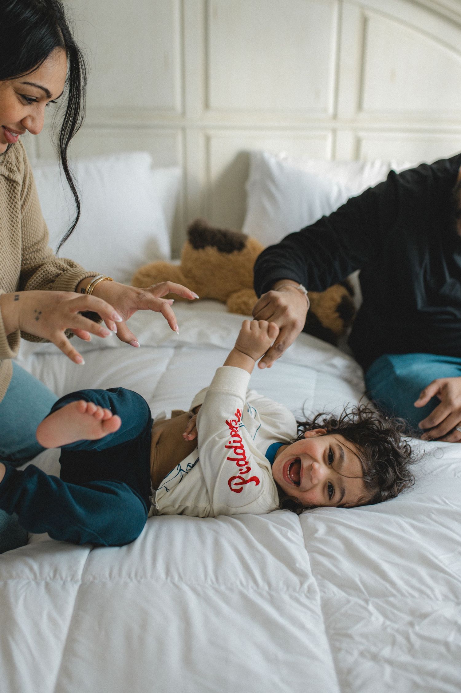 mom dad and son jumping on bed, holding hands, playing, laughing, smiling
