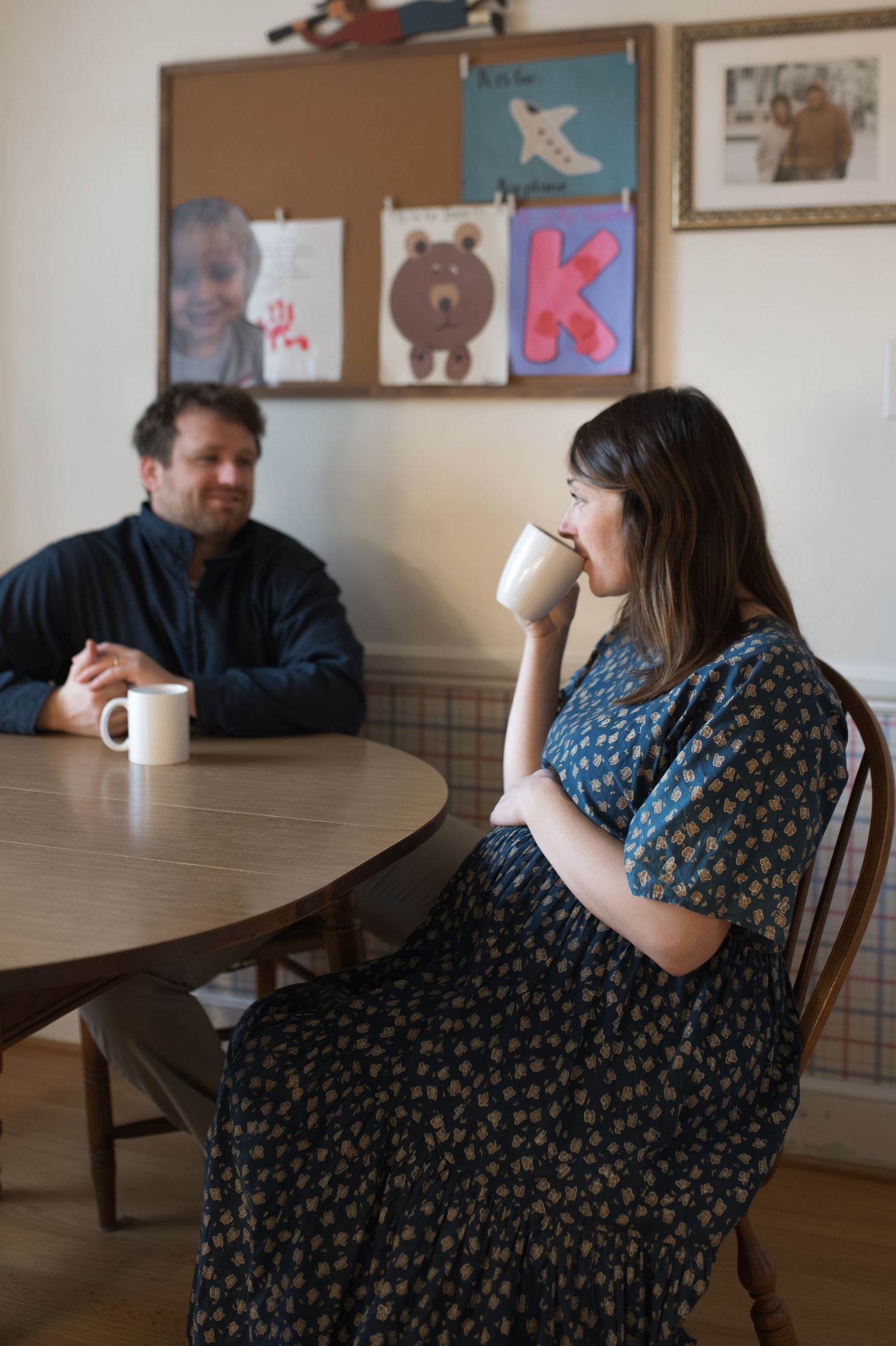 mom and dad drinking coffee at kitchen table. child's artwork on the wall. pregnant mama. at-home documentary maternity session