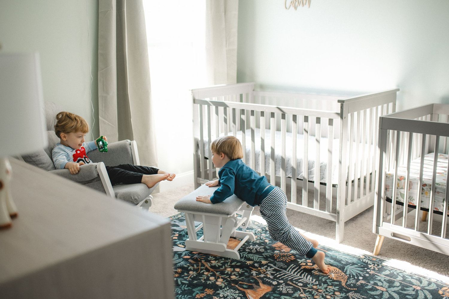 twin boys playing in nursery by crib and newborn twins