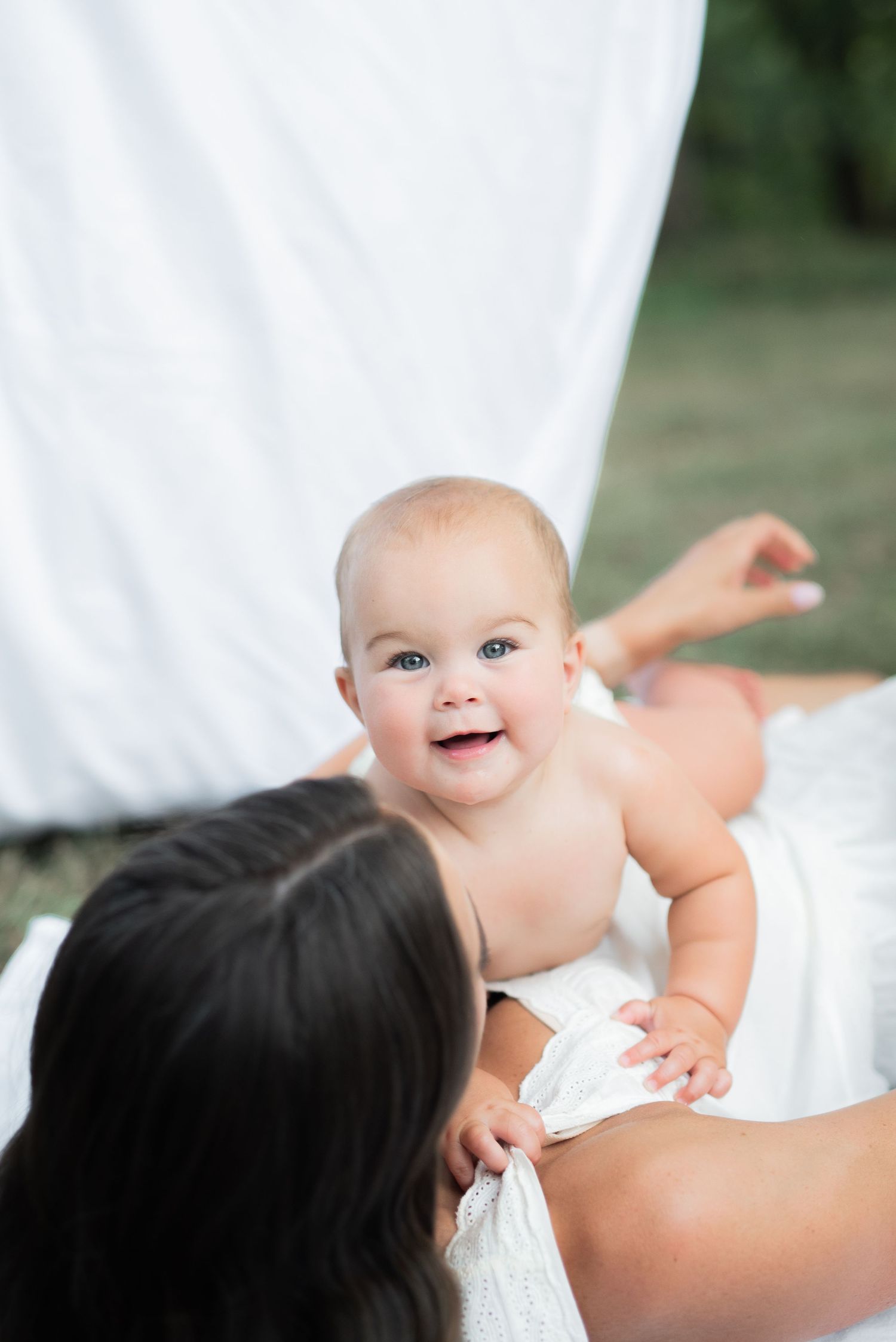 mom and baby outside sitting on white sheet with clothesline hugging