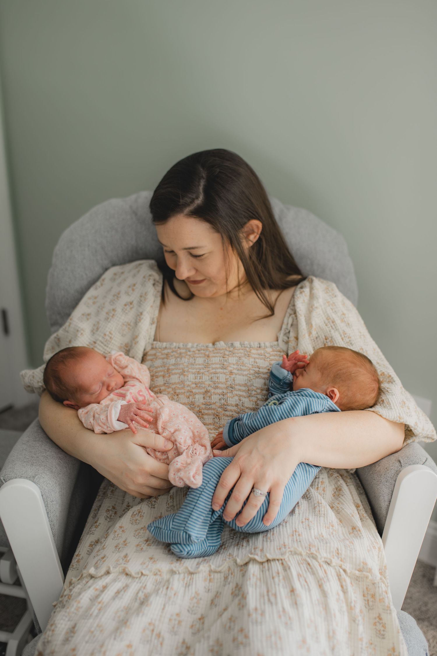 mom holding newborn twin boy and girl sitting in rocking chair In nursery