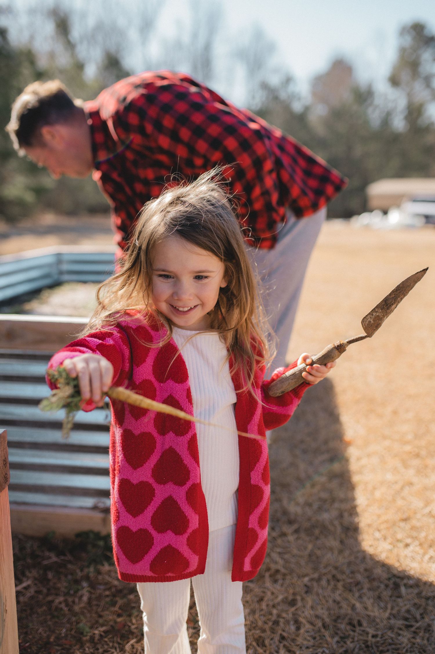 child holding spade and carrots in front of raised garden bed, greenville, nc