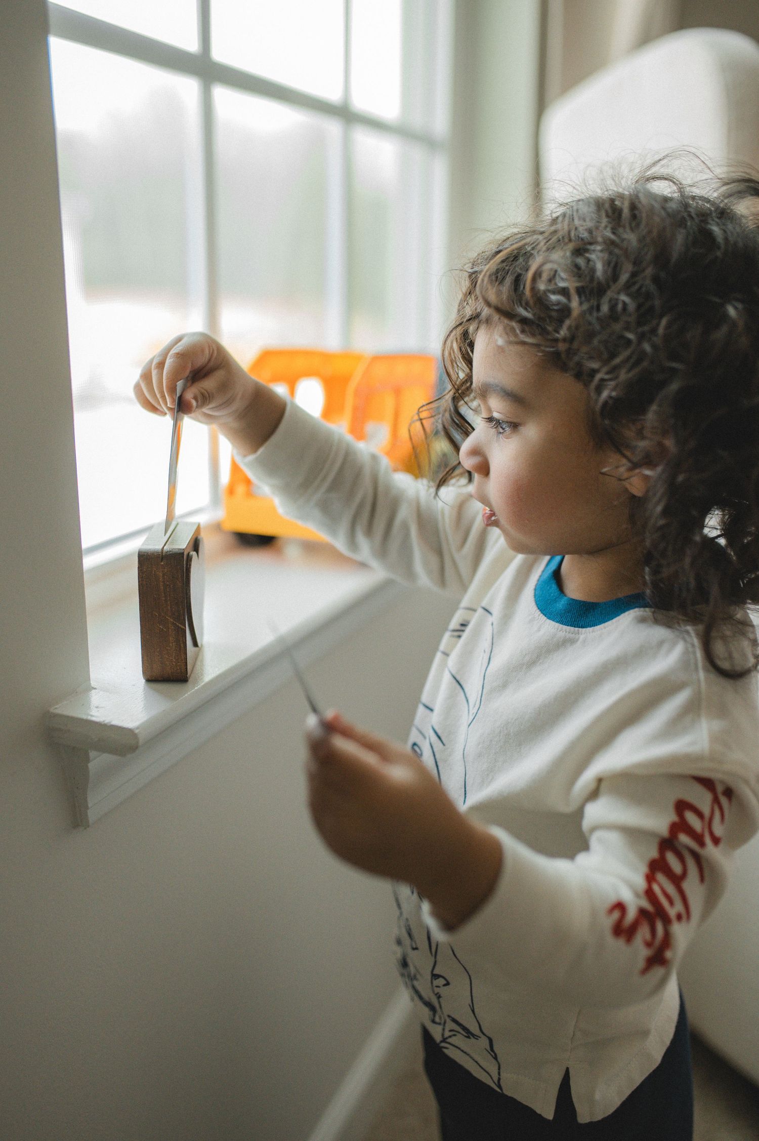 child playing near window, holding polaroid pictures