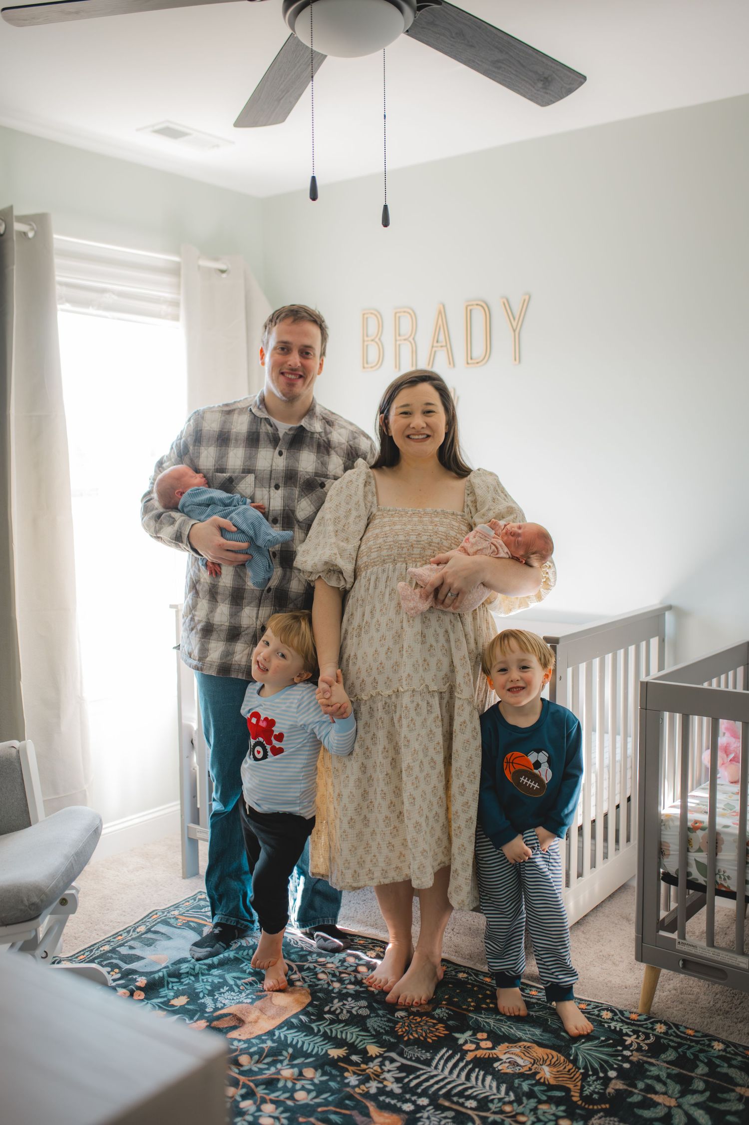 family standing in front of cribs in nursery smiling, greenville nc newborn photographer