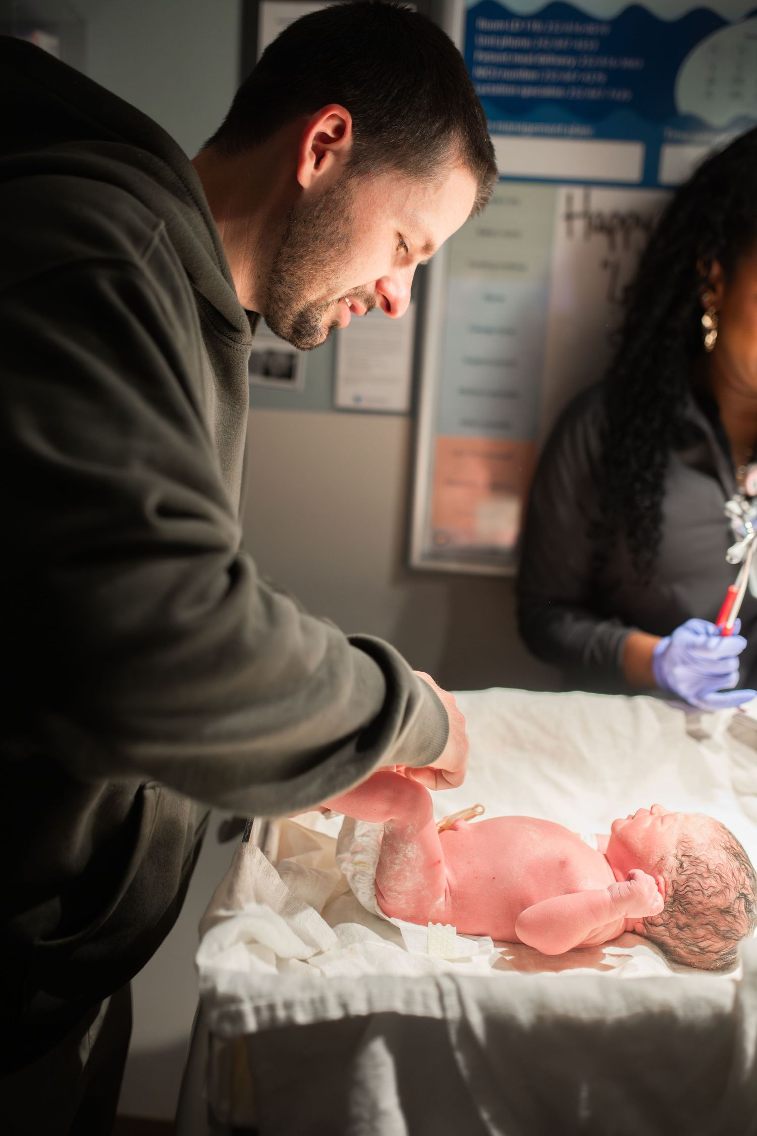 dad changing baby girl's diaper after birth in hospital at ECU Health Medical Center in Greenville NC for the first time